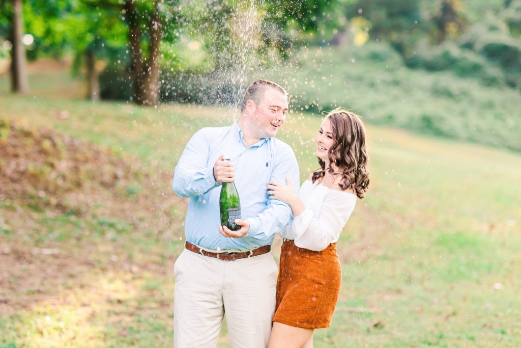 A Couple popping a bottle of champagne at Dorothea Dix Park in Raleigh, NC by Raleigh photographer Tierney Riggs