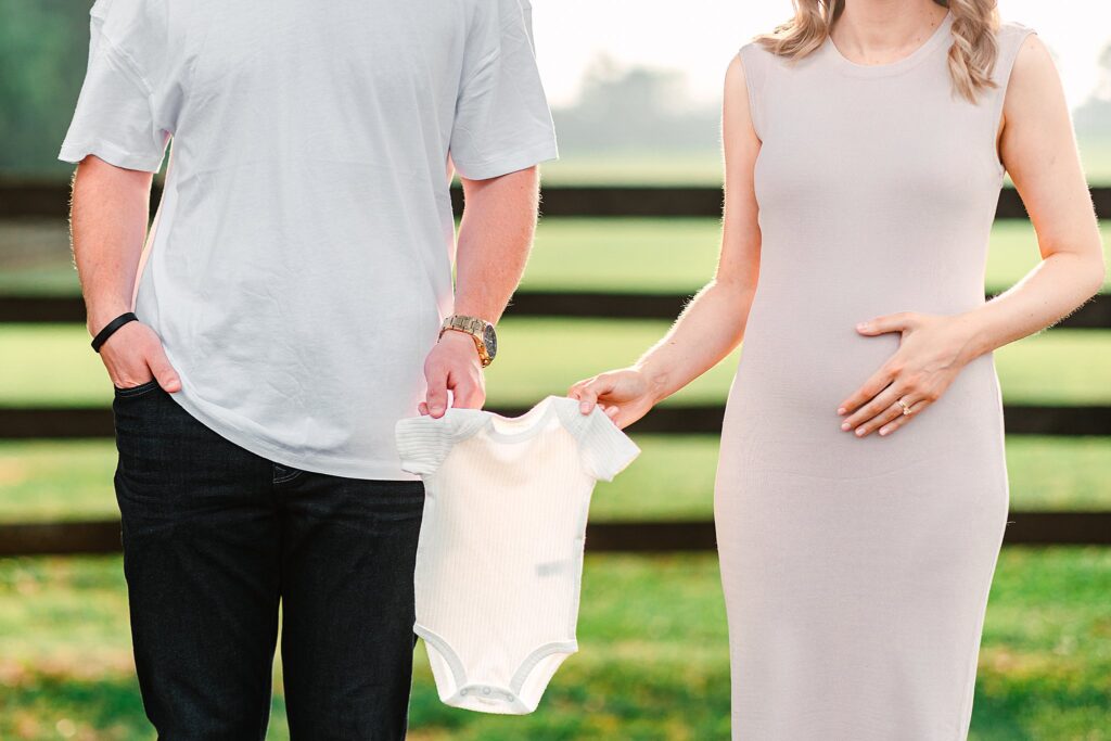 Couple holding a onesie for an a pregnancy announcement photoshoot in Raleigh, NC