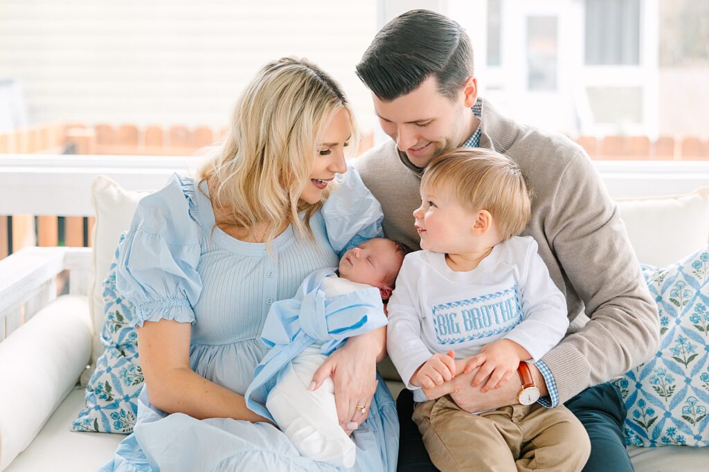 A family snuggled up on the porch swing with their new baby taken by Raleigh newborn photographer Tierney Riggs